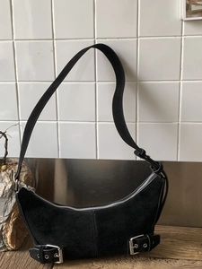 Chic black faux suede half-moon underarm bag with silver hardware on a tiled surface