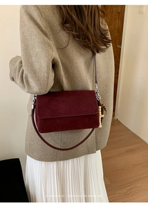 Detail of burgundy suede shoulder bag featuring retro wooden bead charms and flap closure
