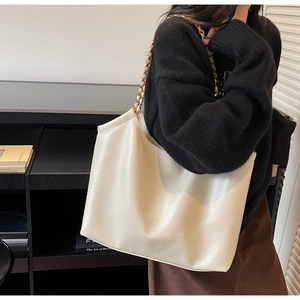 Detail of minimalist cream tote bag showing grainy leather texture and chain strap
