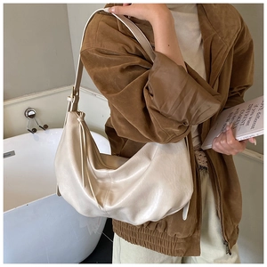 Detail of off-white crescent tote bag featuring soft pleated leather and side tassel accent