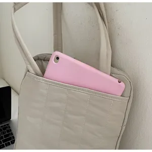 Close-up of beige quilted tote bag showing front pocket storage and padded texture