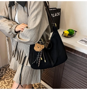 Detail of black suede hobo bag with contrast white stitching and cute bear charm