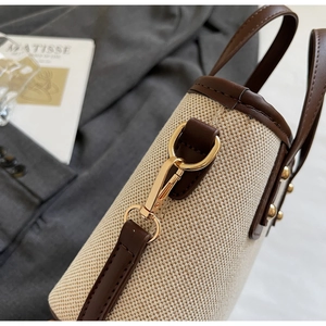Detail of gold metal hook and brown leather trim on beige canvas shoulder bag