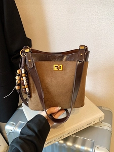 Retro brown suede bucket bag with wooden beads held by hand over a suitcase