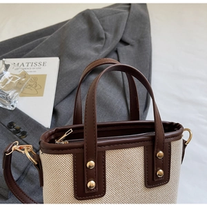 Close-up of contrast stitch handbag with beige canvas, brown leather and gold hardware