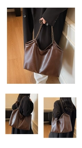 Detailed close-up of large brown leather tote bag with bronze chain strap and soft texture