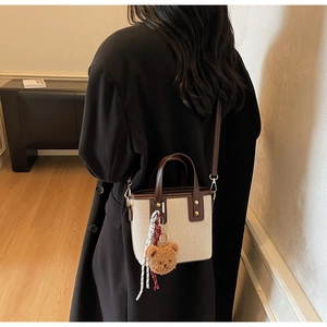 Detail of canvas bucket bag with brown leather trim and cute bear charm worn crossbody