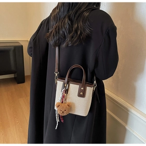 Canvas bucket bag with leather straps and bear charm shown on a female model