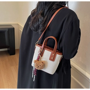 Detailed back view of a canvas crossbody bag with teddy bear charm on a black coat