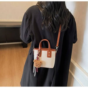 Back view of a crossbody bucket bag in cream canvas and brown leather with bear charm