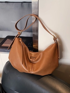 Brown soft faux leather hobo tote bag with a slouchy crescent shape on a leather chair