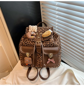 Close-up of leopard print backpack featuring brown leather accents and plush charms