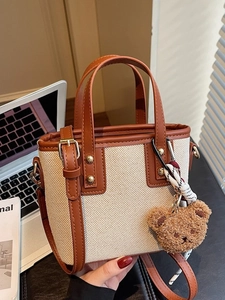 Mini canvas handbag with brown leather trim and cute plush bear charm in a lifestyle setting