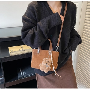 Detail of brown suede crossbody bag featuring cute bear charm and striped tassel accent