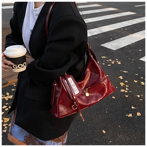 Detail of burgundy glossy leather hobo bag with gold hardware on an urban street