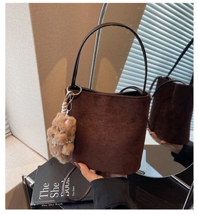 Détail d'un sac seau en daim marron orné d'un petit ours en peluche sur la lanière
