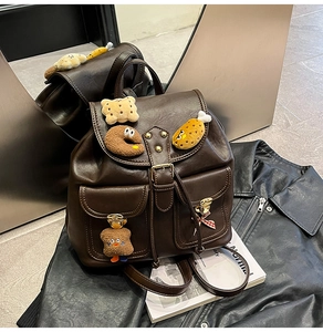 Detail of a brown leather backpack with dual front pockets and cute plush accessories