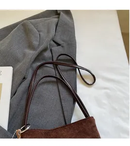 Détail du sac seau en daim marron foncé avec fines bandoulières et anneaux métalliques