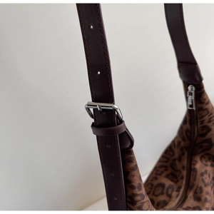 Detail of adjustable burgundy leather strap and metallic buckle on leopard print tote bag