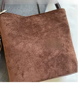 Détail macro du sac seau en daim marron foncé montrant le tissu mat doux et les coutures
