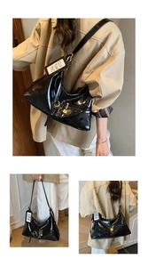 Detail of glossy black patent leather shoulder bag with white branded tag and gold hardware