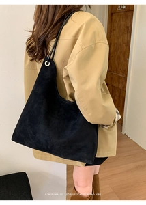 Close-up of minimalist black suede bucket bag with fine shoulder straps and matte finish