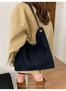 Minimalist black faux suede hobo bag shown on shoulder over a beige trench coat