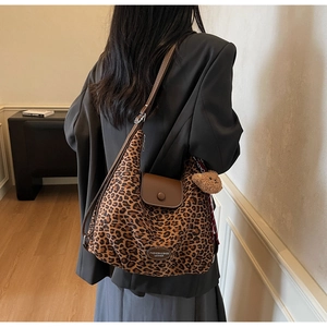 Detail of leopard print tote bag with leather strap and plush bear charm on model