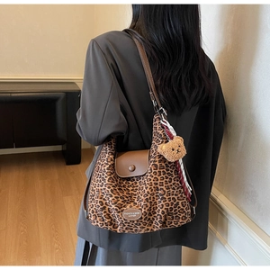 Detail of leopard print canvas tote bag featuring brown leather flap and bear charm