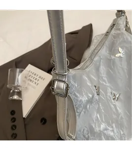 Detail of silver metallic crinkled bag with butterfly metal buckle and adjustable strap