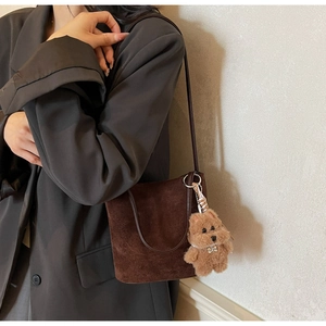 Détail d'un sac seau en daim marron foncé avec un charmant accessoire chien en peluche
