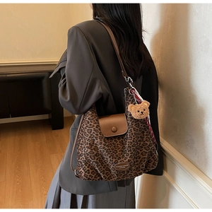 Detail view of large leopard print tote bag with brown leather flap and bear charm accessory