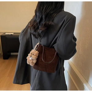 Détail du sac seau en daim marron avec charme de chien en peluche sur un blazer gris