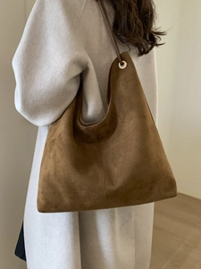 Deep brown suede bucket bag with long shoulder strap shown on a model for daily commute
