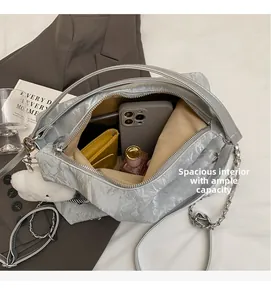 Detail view of silver pleated shoulder bag interior holding phone, wallet and perfume