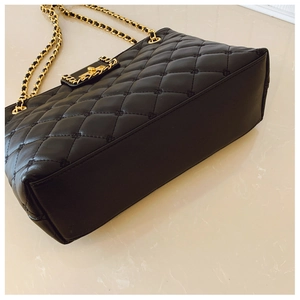 Detail of black quilted shoulder bag featuring gold chain strap and elegant stitching