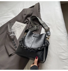 Close-up of black bucket bag with textured leather and wide geometric fabric strap