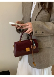 Detail of burgundy leather handbag featuring suede flap and retro gold hardware clasp