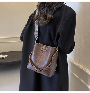 Brown bucket bag featuring a decorative woven chain and a wide ethnic jacquard strap