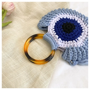 Close-up of crochet Evil Eye handbag with blue knit texture and amber resin handle