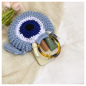 Detail of hand-woven crochet bag with evil eye pattern and resin ring handle with tassel