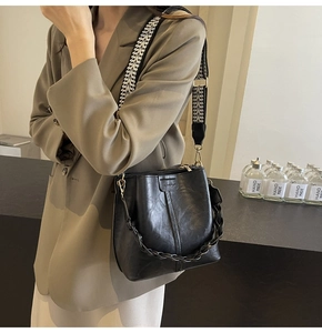 Detail of black leather bucket bag with geometric wide strap on a brown blazer outfit