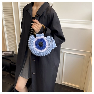 Close-up of handmade crochet evil eye handbag with amber resin handle and blue tassels