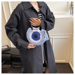Detail of hand-woven crochet bag with evil eye pattern and resin ring handle