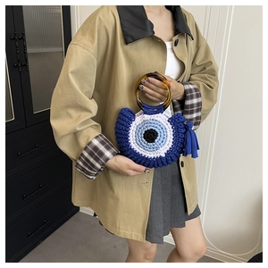 Detail of hand-woven evil eye crochet bag with blue tassel and amber round handle