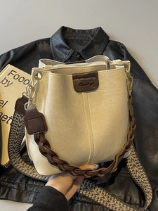 Cream bucket bag with brown leather trim, woven handle and wide ethnic shoulder strap