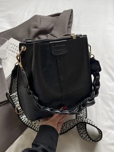 Classic black leather bucket bag with geometric wide strap and gold hardware on white background