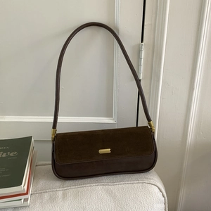 Detail of dark brown baguette bag featuring suede flap and golden metal clasp