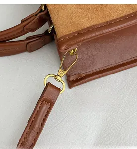 Detail of golden metal hook and stitching on brown leather and suede tote bag