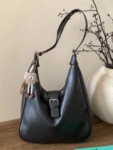 Sac hobo rétro noir avec boucle argentée et breloque en peluche sur un bureau en bois